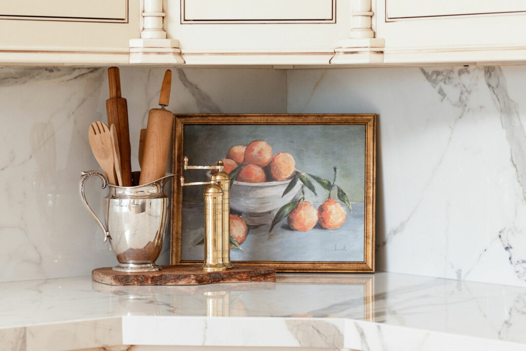 Nancy Meyers aesthetic white marble backsplash, oranges picture, wooden spoons, brass salt and pepper mills