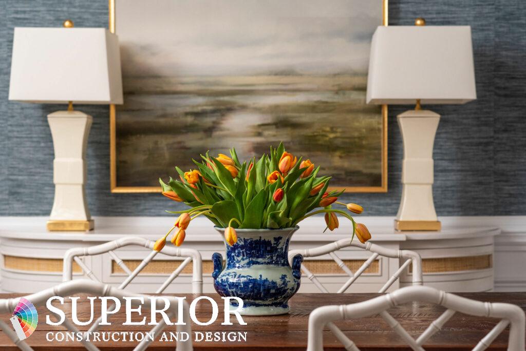 Nancy Meyers aesthetic dining room with bamboo furniture, rattan sideboard, cream ceramic lamps, blue grass cloth and nature-inspired artwork